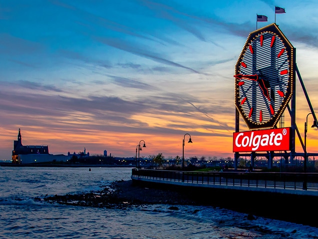 merenranta, taustalla Colgate-logo suuren kellon alla, jossa on punaiset osoittimet