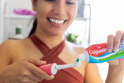 Nainen hymyilee, kun hän laittaa Colgate-hammastahnaa hammasharjaan kylpyhuoneessa.